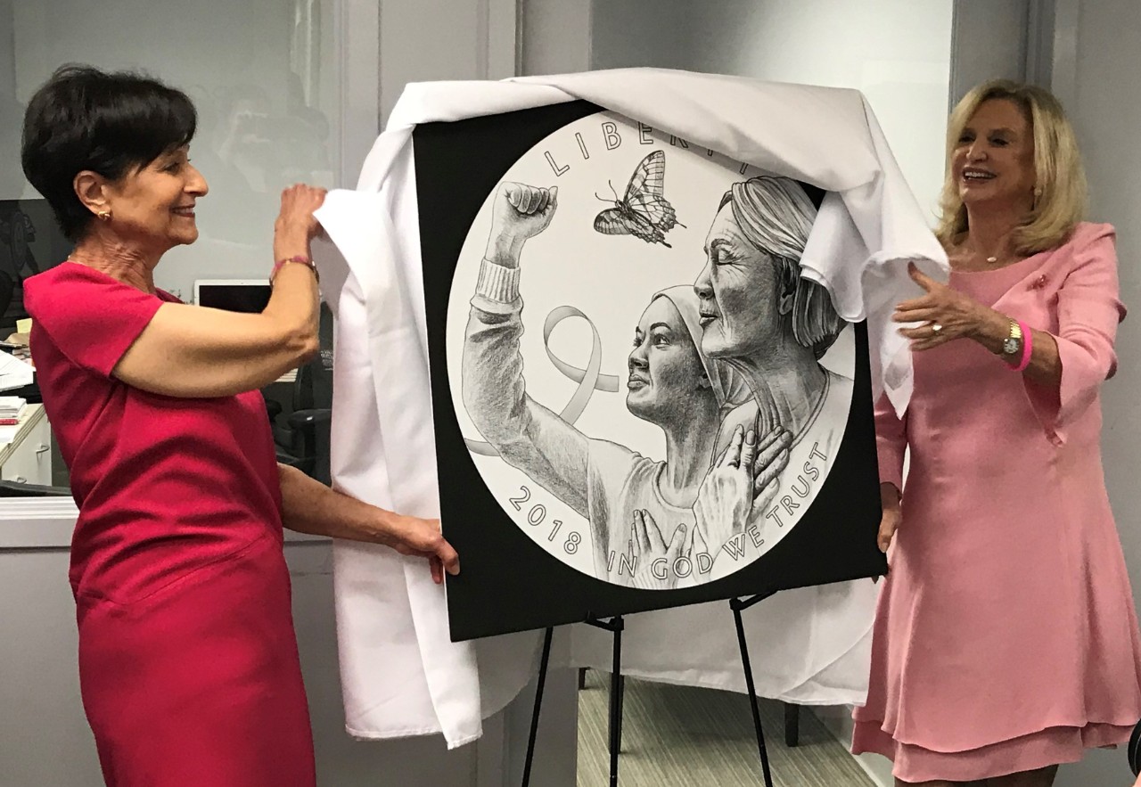 two women removing a cover from a coin design poster