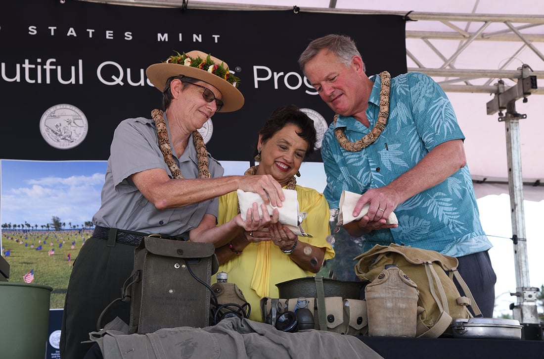 Director David Ryder, Governor Lourdes Leon Guerrero, and Superintendent Barbara Alberti pour coins into a WWII helmet
