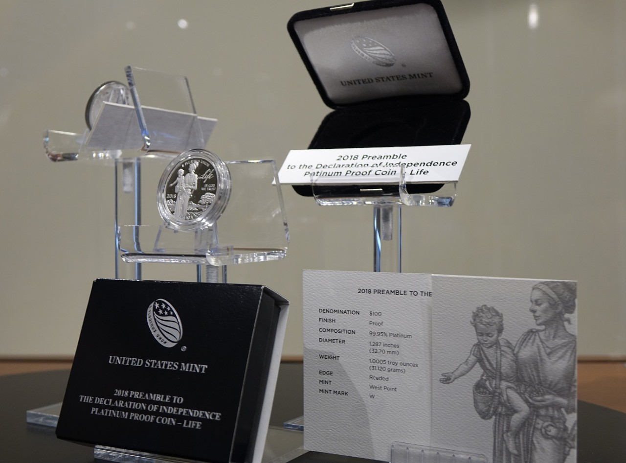 black and silver packaging, a platinum proof coin, and line art showing liberty holding a child