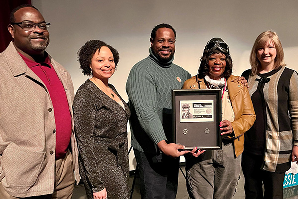 five people standing in a line with two of them holding a shadow box frame