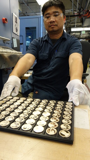Hai Xiao, a die setter at the United States Mint at San Francisco, places a tray of newly minted President Gerald Ford proof coins in a stack before sending them to get packaged. 