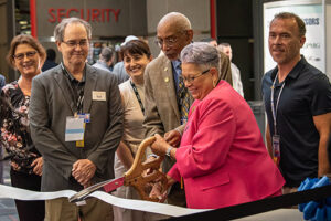 U.S. Mint director, ANA president, and others hold large scissors cutting a ribbon